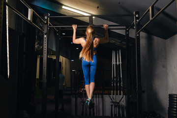 Fototapeta na wymiar strong muscula girl with ponytail exercises pulling up. full length back view photo. woman practising strength training in the fitness center. full length back view photo