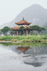Traditional Vietnamese ancient temple with green mountains on background reflecting in water, Ninh Binh province, Vietnam