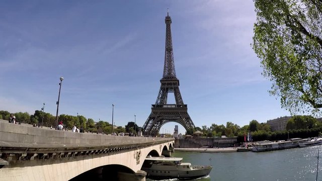 wide shot of Eiffel Tower in Paris Francewith bridge over Seine River boat passes under bridge-people on bridge-sunny day-blue sky