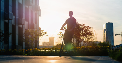 Man riding black electric kick scooter at cityscape background at sunset