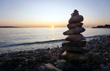 Stacking stones on the empty pebble beach at summer sunset