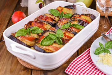 Traditional italian food. Eggplant and tomatoes with parmesan. Baked summer wax with sauce, cheese and basil. Healthy lunch for the family.