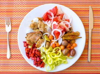 Top view of plate full with pork meat and vegetables, olives, paprika, tomatoes, baby carrots and onions