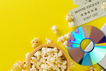 Movie tickets, DVD or blu ray disc and popcorn on yellow table background. Home theatre movie or...