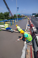 Group of construction workers finishing concreting  sidewalk on the bridge during traffic hours