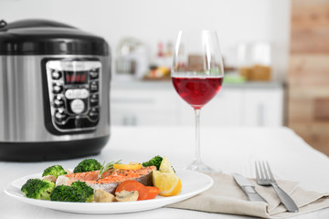 Plate with salmon steak and garnish prepared in multi cooker on table