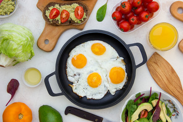 Pan of fried eggs with tasty vegetarian sandwich with avocado, egg, tomato on wooden board.