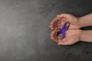 Woman holding purple awareness ribbon on grey background, top view with space for text