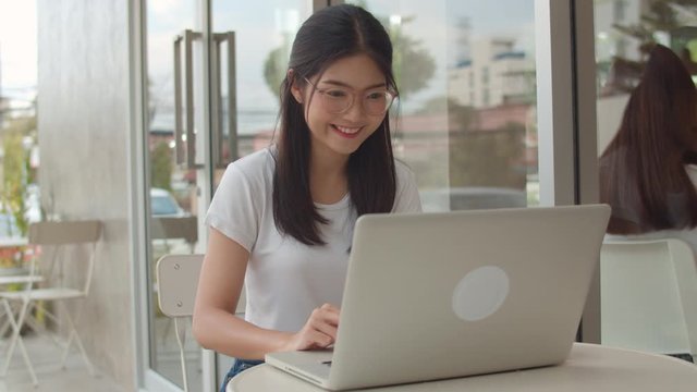 Freelance Asian women working on laptop at coffee shop. Young Asia business Girl using computer for trade, send email, digital work on internet on table at outdoor cafe in evening concept. Slow motion