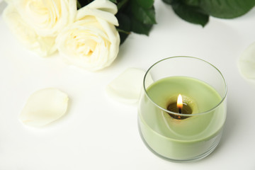 Burning candle in glass holder and roses on white table, space for text