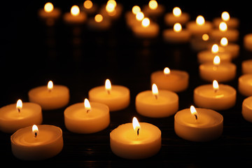 Many burning candles on black table in darkness