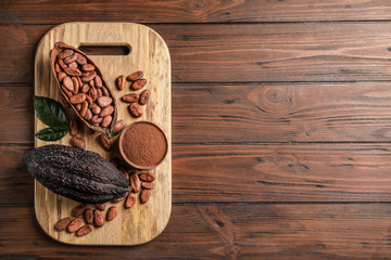 Board with cocoa pods, beans and powder on wooden table, top view with space for text