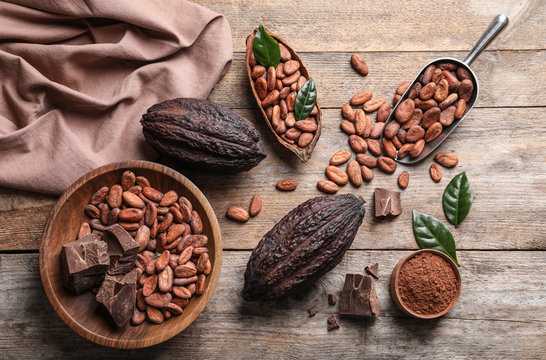 Flat lay composition with cocoa beans, chocolate pieces and pods on wooden table