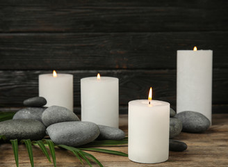 Fototapeta na wymiar Burning candles, spa stones and palm leaf on wooden table