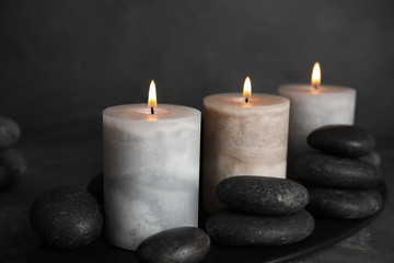 Fototapeta na wymiar Burning candles and spa stones on black plate, closeup