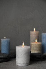 Fototapeta na wymiar Burning candles and spa stones on grey table, space for text