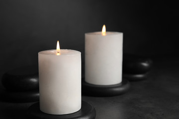 Fototapeta na wymiar Burning candles and black spa stones on grey table