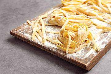 Board with uncooked egg noodles and flour on grey table, closeup