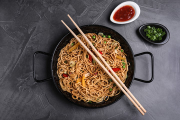 Cooked noodles with vegetables served on grey table, flat lay