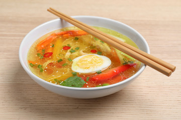 Bowl of tasty ramen with noodles, vegetables and chopsticks on wooden table