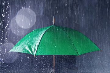 Bright umbrella under rain on dark background