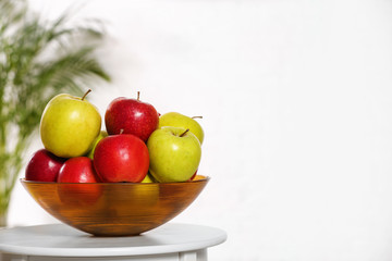 Bowl with different sweet apples on table indoors, space for text