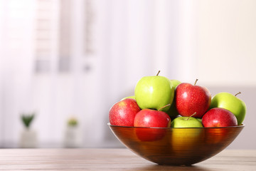 Bowl with different sweet apples on table in room, space for text
