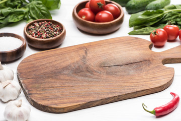 selective focus of cutting board, cherry tomatoes, greenery, garlics, pepper, cucumbers, salt and...