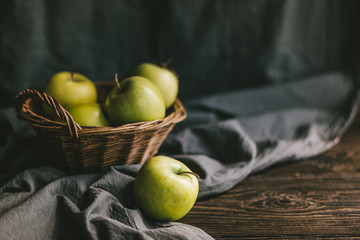 Ripe green apples in a basket on wooden table with cloth.
