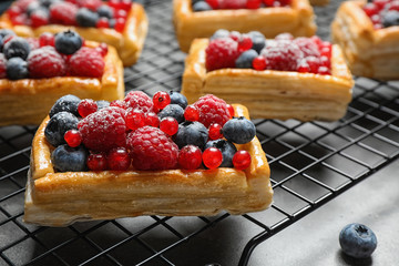 Cooling rack and fresh delicious puff pastry with sweet berries on grey table, closeup
