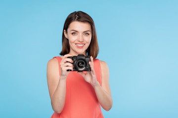 Happy young woman with toothy smile holding camera in front of her