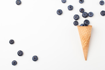 Ice cream cone filled with blueberries on a white background. Berries fall out from a waffle cone. Copy space