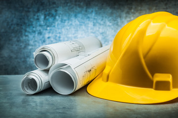constrution helmet rolled blueprints on metalic background