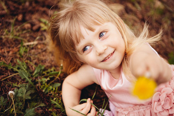 Beautiful little girl smiling with yellow dandelion flower in hand, portrait of child