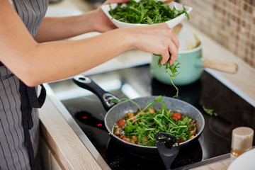 Close up of Caucasian woman standing in kitchen next to stove and preparing healthy vegetarian dinner.