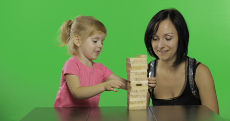 Mother and daughter plays the jenga. Child pulls wooden blocks from tower