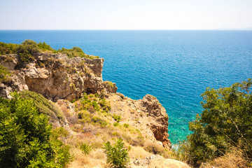 Beautiful view from the cliff of the sea. The water is clear with a blue tint. Bushes and various vegetation grow on the rock.