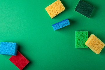 Scattered yellow, green, red, blue sponges on green colored paper background, copy space, top view, flat lay