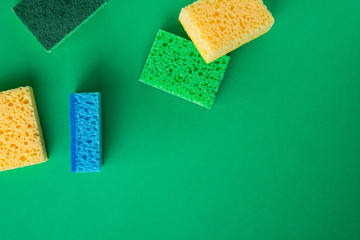 Scattered yellow, green, blue sponges on green colored paper background, copy space, top view, flat lay