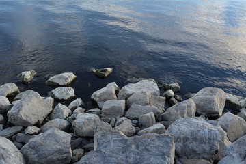 Grey stones near blue water of rhe river.