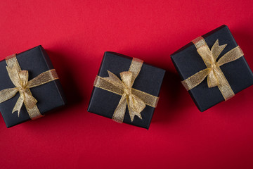 Three black gift box with golden ribbons in line on red paper background, texture, isolated, top view, flat lay, copy space
