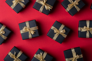 Black gift box with golden ribbons on red paper background, pattern, texture, isolated, top view, flat lay