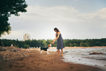 Fototapeta na wymiar Image of happy woman 20s hugging her dog while walking along the beach