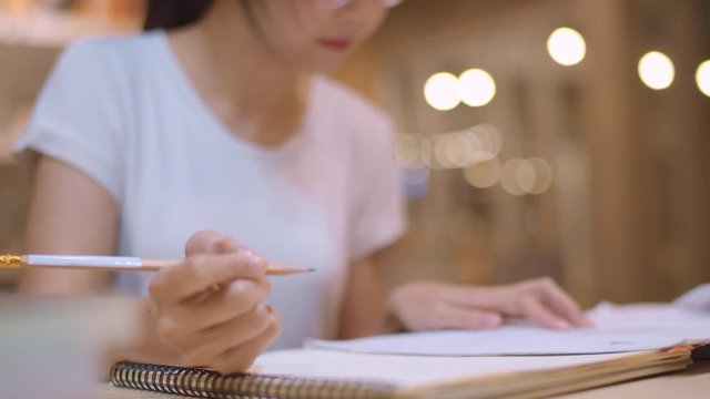 Asian student women reading books in library at university. Young undergraduate girl do homework, read textbook, study hard for knowledge on lecture desk at college campus overtime night. Slow motion.