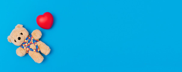 World Autism Awareness day, mental health care concept. Teddy bear with red heart and ribbon puzzle pattern. On blue background