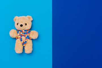 World Autism Awareness day, mental health care concept with teddy bear and ribbon puzzle pattern. On blue background.