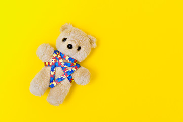 World Autism Awareness day, mental health care concept with teddy bear and ribbon puzzle pattern. On yellow background.