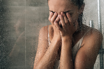 upset sad woman covering face and crying in shower at home