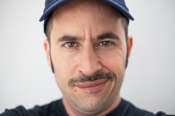White male with a prominent mustache and a hat against a seamless background looks at the camera