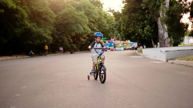 Child riding bicycle in park at sunset light. Kid in helmet learning to ride at summer. Happy boy riding bike, having fun outdoors on nature. Active sport family leisure. Healthy holidays. Slow motion